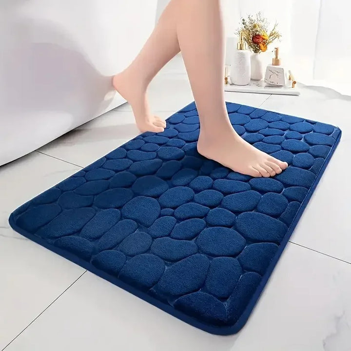 Navy blue textured bath mat with feet stepping onto it on a light-colored floor.