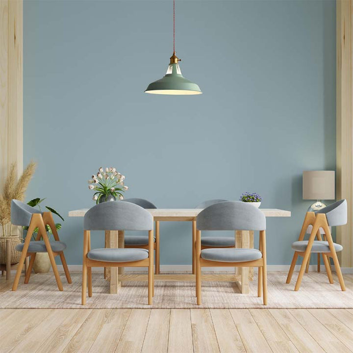 Dining room with retro industrial green pendant light over a table and chairs against a light blue wall.