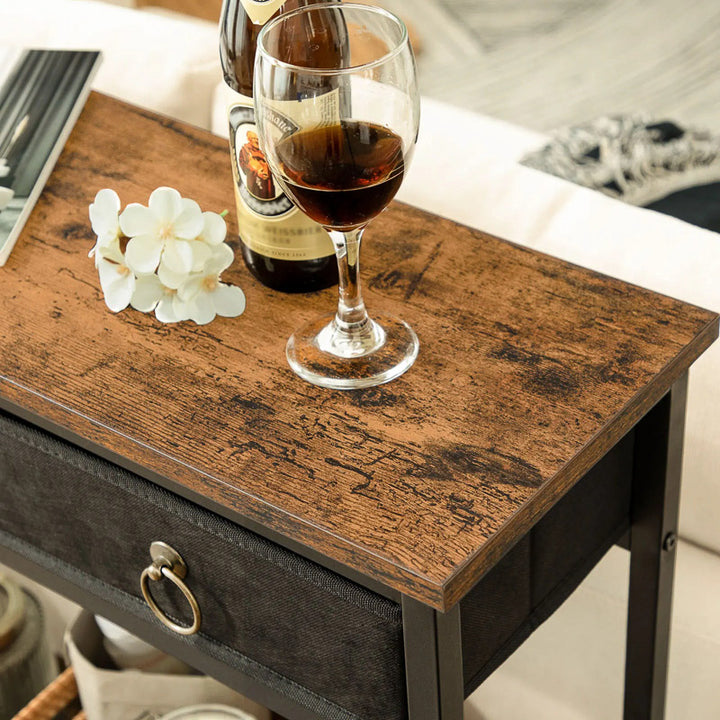Wooden side table with a glass of dark liquid, bottle, and decorative flowers.