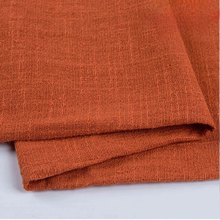 A set table featuring rustic orange cotton napkins, with plates, glasses, and decorative elements in the background.