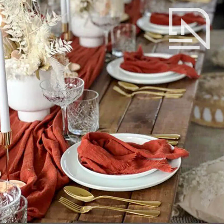 Decorative table setting with red napkins, gold cutlery, and white plates on a wooden table.