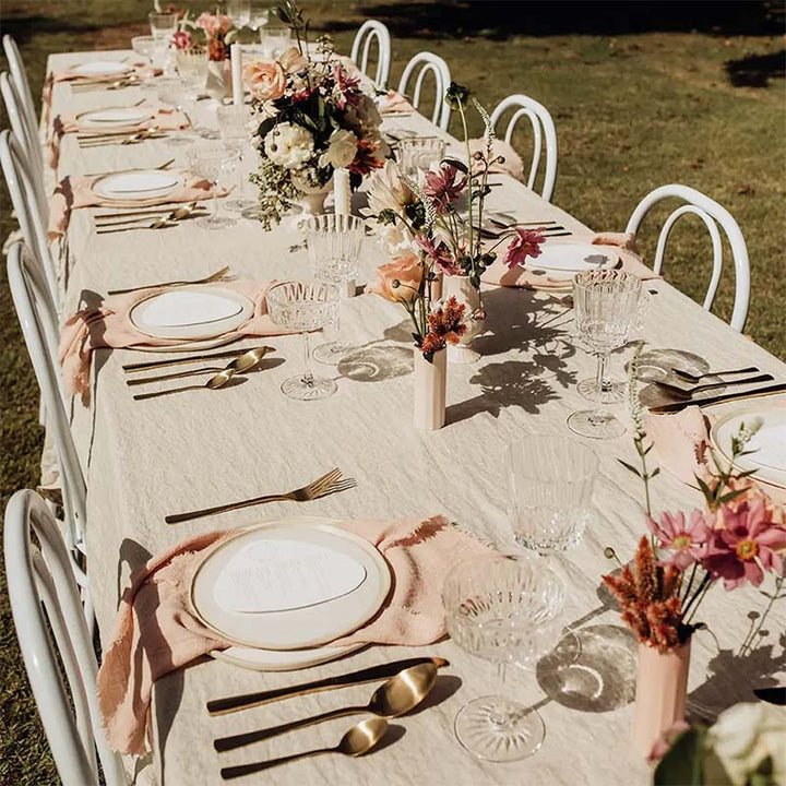 Elegant outdoor dining table setting with floral centerpieces, cotton napkins and white chairs.