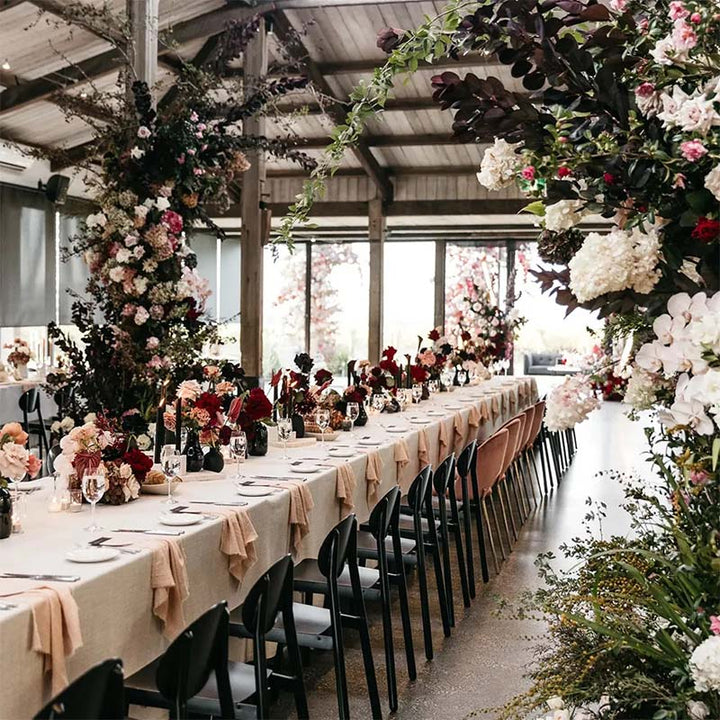 Long table set for a wedding reception with floral decorations , rustic, cotton napkins and chairs.