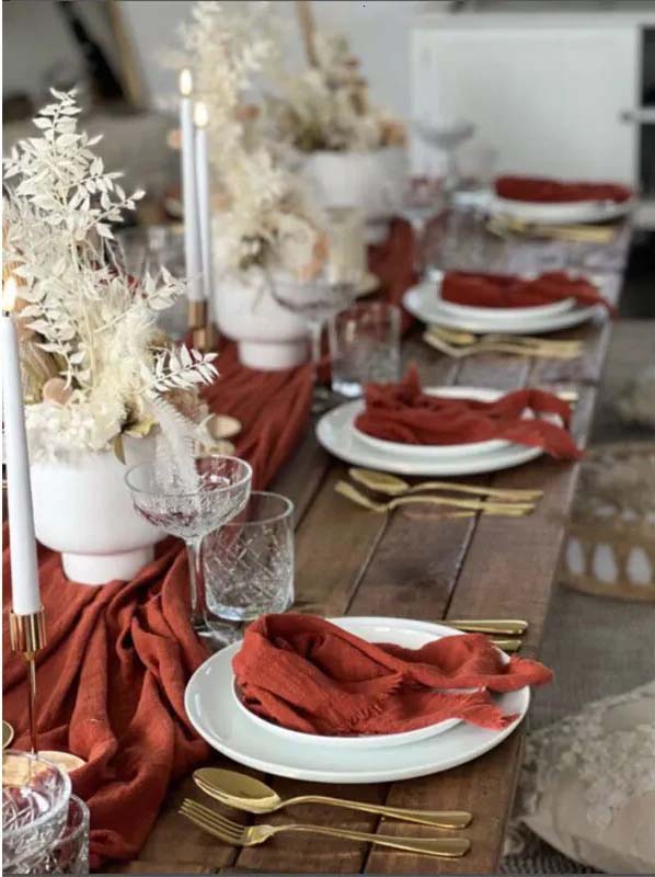 Elegant table setting with red napkins, gold cutlery, and white plates on a wooden table.