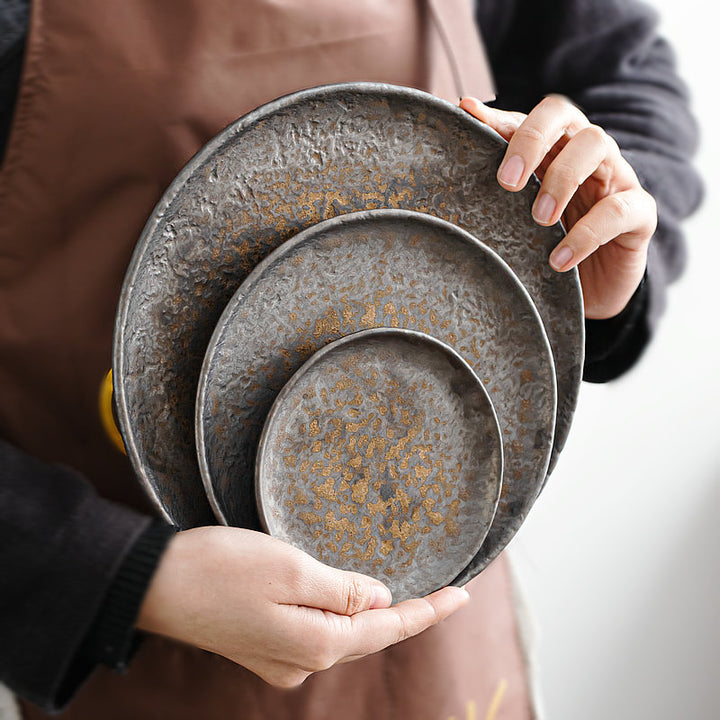Person holding three nested grey rustic stoneware shallow ceramic serving plates, 22/17/12 cm