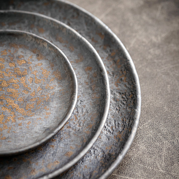 Close-up of stacked shallow ceramic serving plates in rustic grey stoneware, 22/17/12 cm