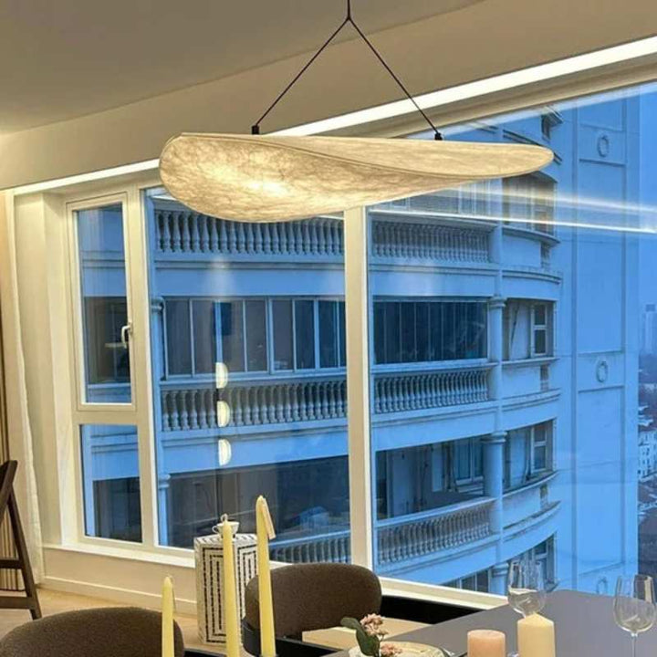 Pendant light with delicate silk shade, suspended in front of a cityscape window view.