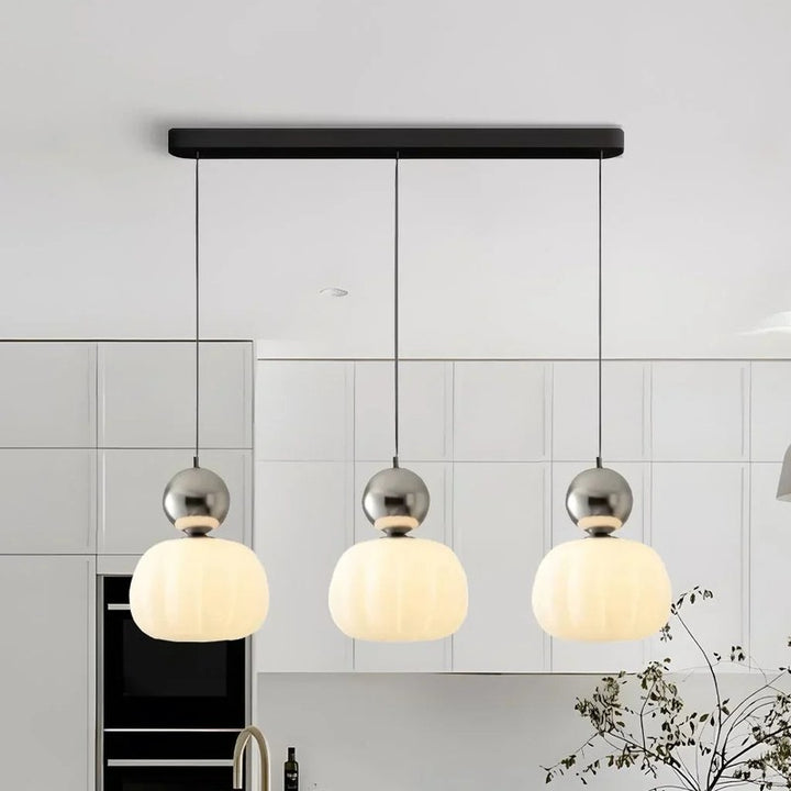 Trio of chrome-accent Art Deco pendant lights with white glass shades above modern kitchen island