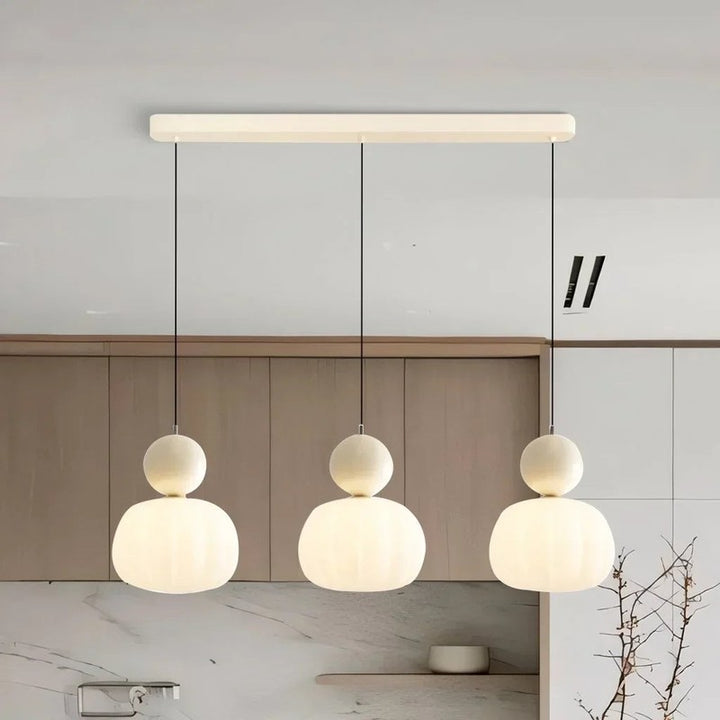 Three cream-accent Art Deco pendant lamps in a row, softly glowing in minimalist kitchen setting