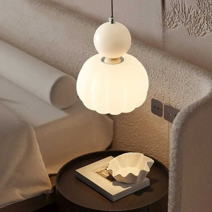 Cream Art Deco pendant lamp with scalloped glass shade, glowing beside a bedroom nightstand