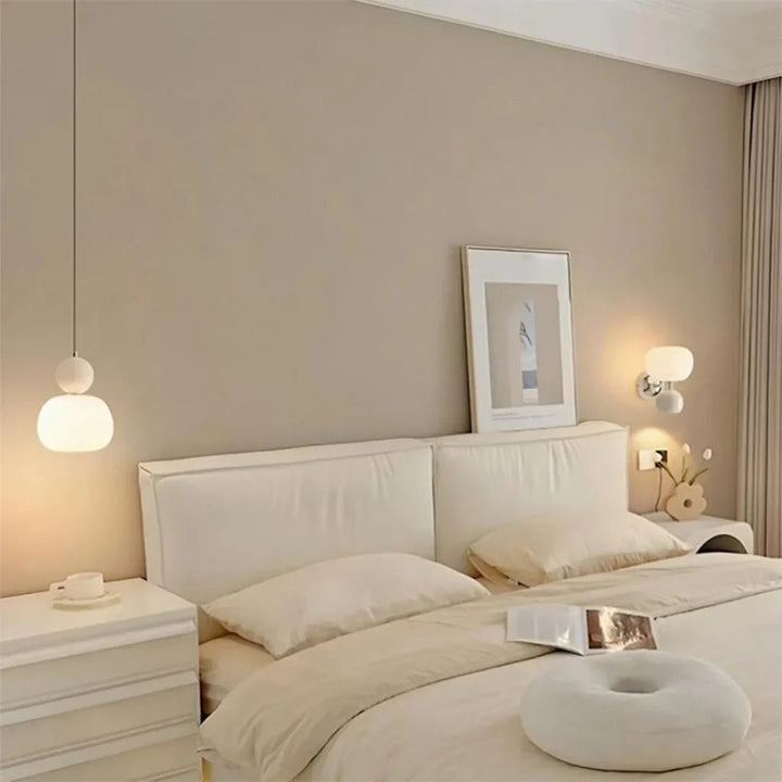 Minimalist cream pendant lamp softly illuminating a beige bedroom with white bedding
