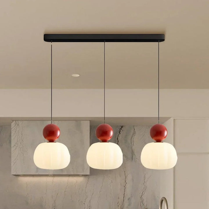 Trio of red-accent Art Deco pendant lights in a row above a modern kitchen island