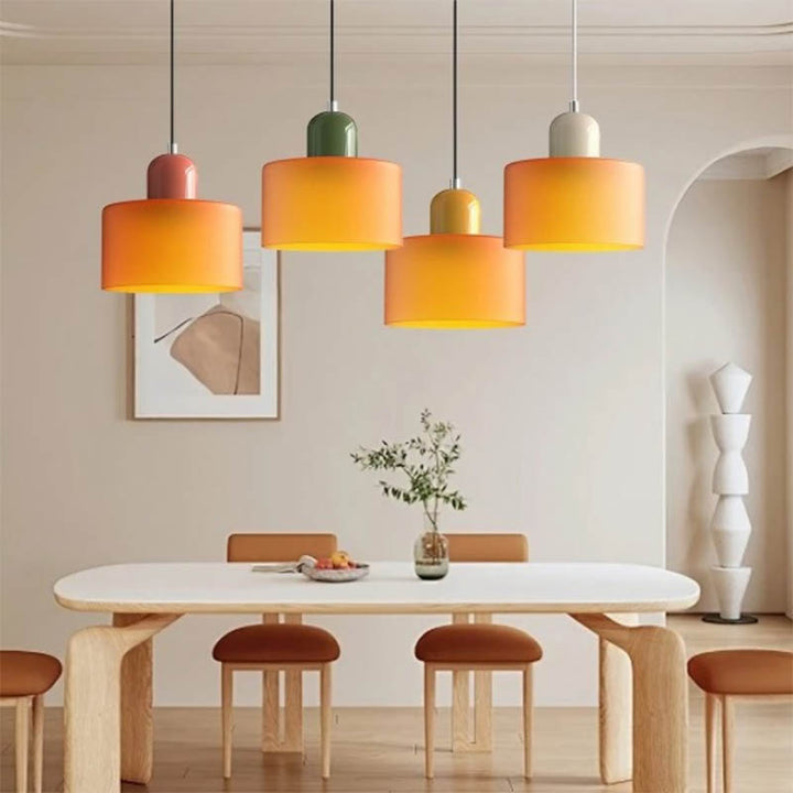 Four multicolour Nordic pendant lights in orange, yellow, and green above a wooden dining table in a Scandinavian-style space.