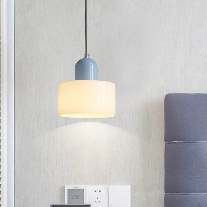Blue and pale amber Nordic glass pendant light mounted on a light grey wall, softly glowing above a bedside table.