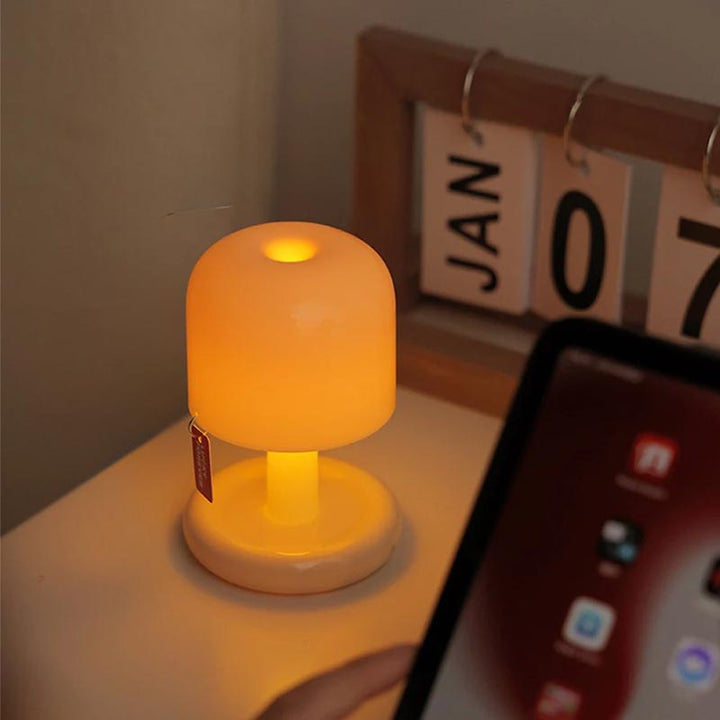 Rechargeable mushroom table lamp on a wooden desk beside a calendar, creating warm ambient desk lighting.