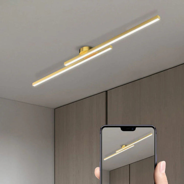 Gold aluminium LED strip ceiling light fixture shown in modern bedroom with smartphone reflection.