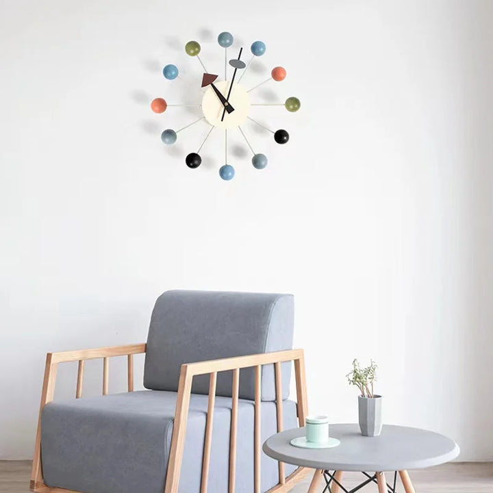 Scandinavian silent wall clock with colourful wooden balls displayed above modern grey armchair