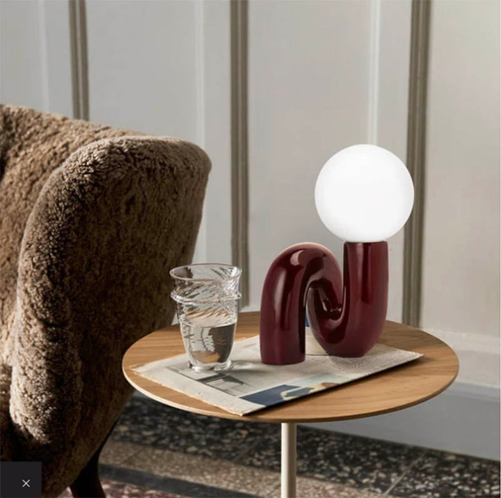 Scandi-style LED lamp on side table, featuring a burgundy resin swirl base and round white glass shade for cosy UK interiors.