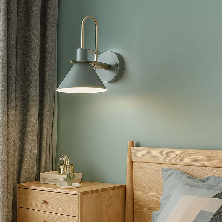 Wall-mounted lamp on a green wall with a wooden nightstand and bed in the foreground