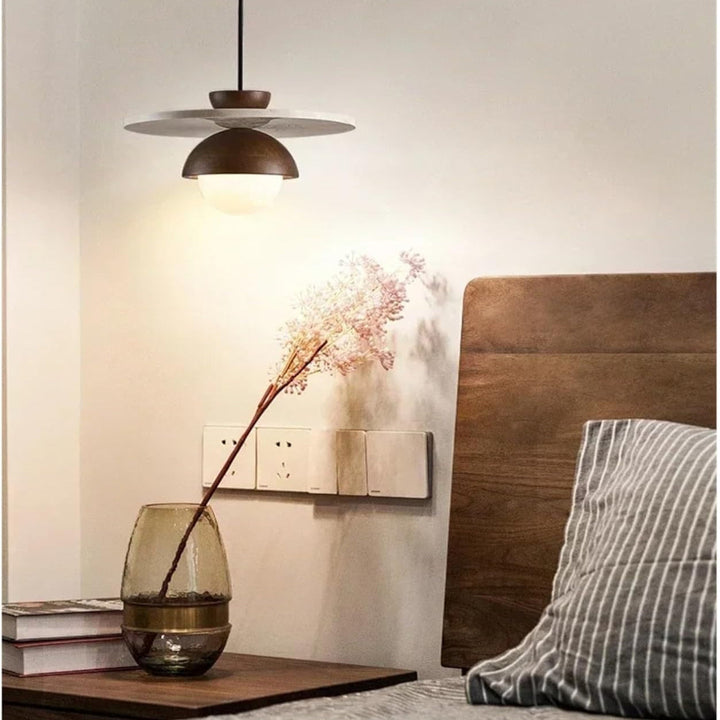 Modern pendant light fixture in a bedroom setting with a vase and books on a nightstand.