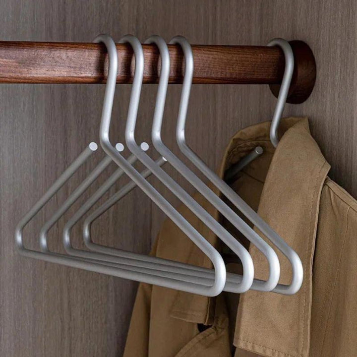 Set of matte silver aluminium hangers on wooden rod, sleek and durable closet organisers for coats or shirts.