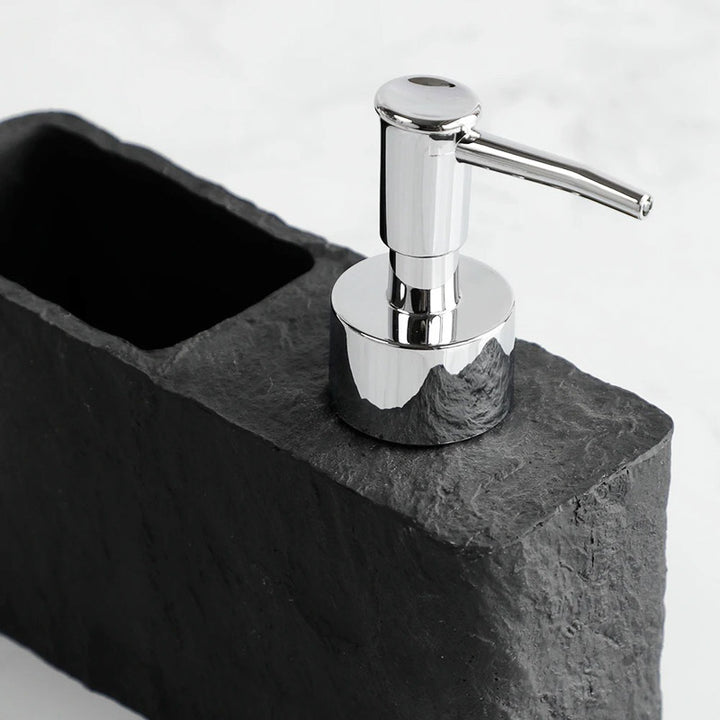 Silver soap dispenser on a dark stone surface with a white background