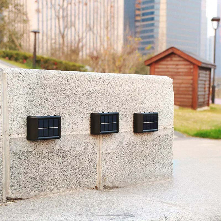 Black solar fence light installed on outdoor wall, charging via sunlight for automatic night activation.