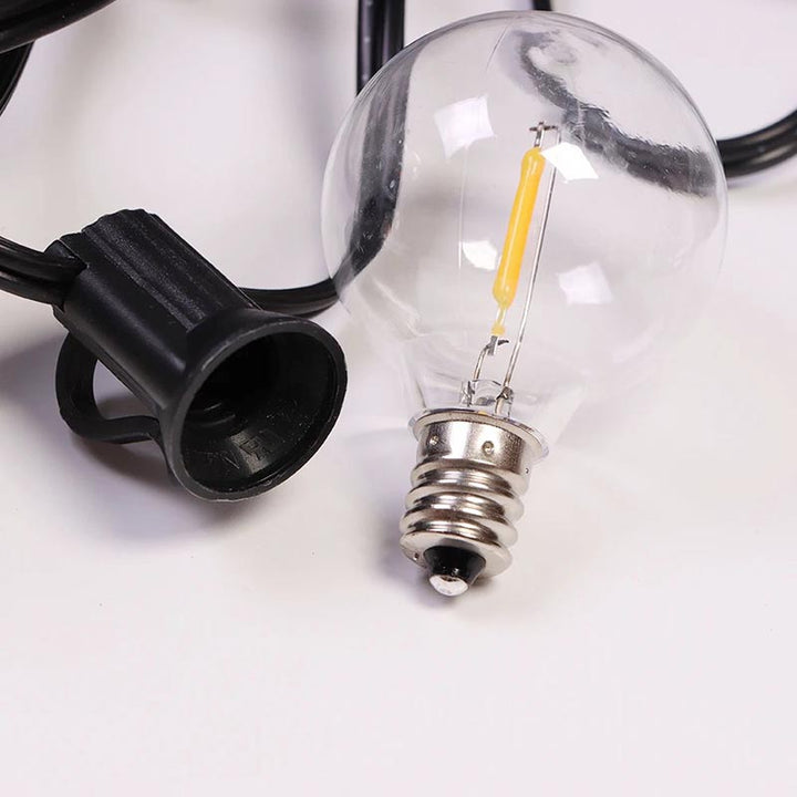 Clear shatterproof LED bulb on black solar string light cable, perfect for outdoor garden or patio use.
