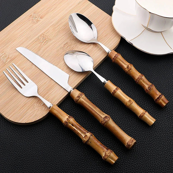 Set of silver cutlery with bamboo handles on a wooden board.
