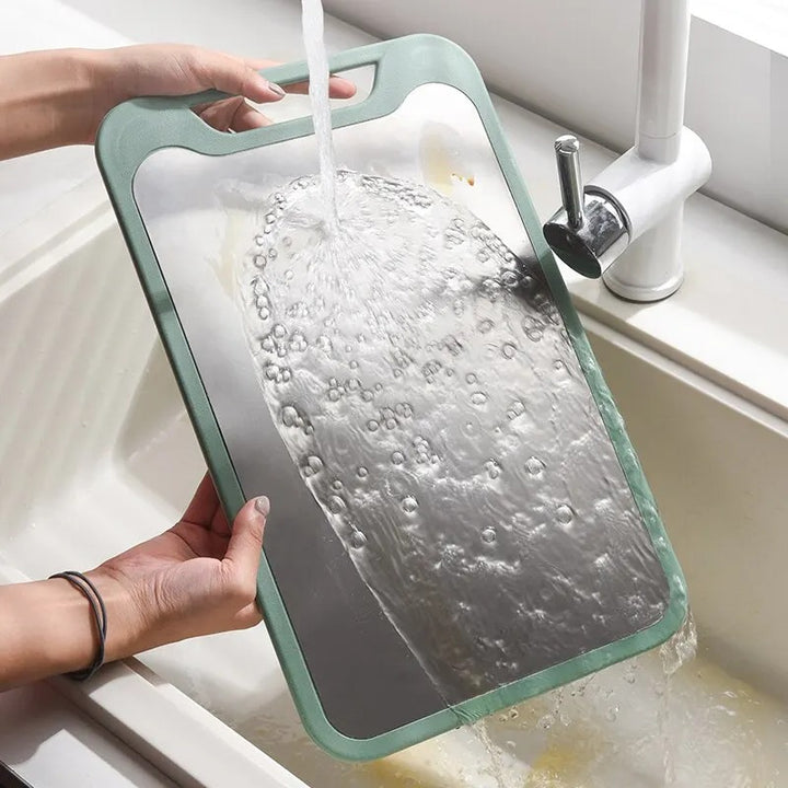 Person washing a cutting board under running water in a sink.