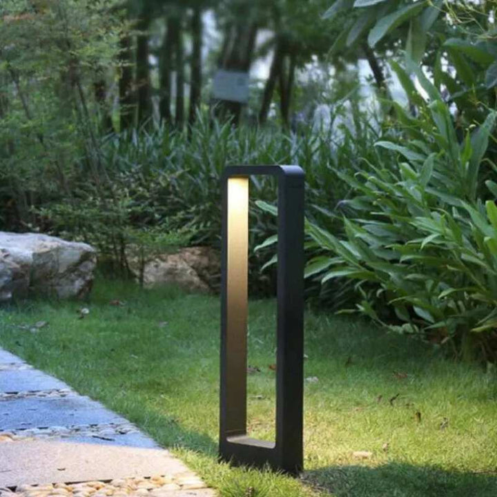 Garden light fixture on a grassy area with plants and rocks in the background