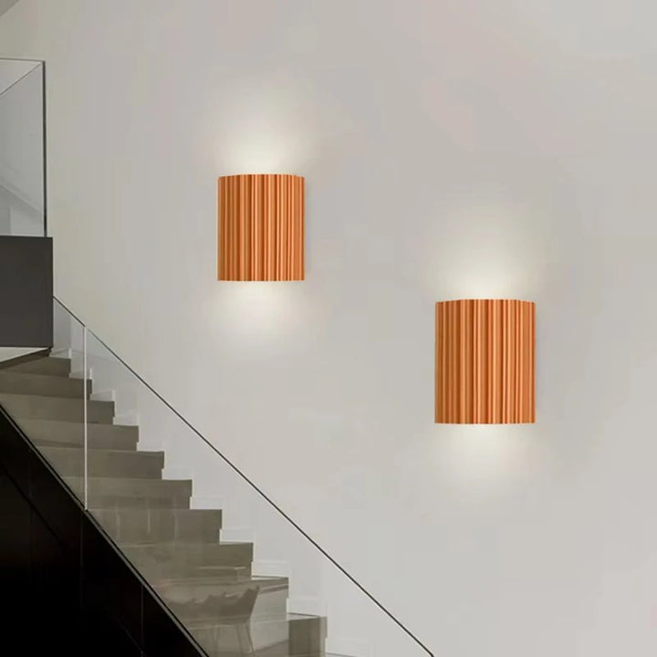 Two wall-mounted lamps with resin shades on a white wall next to a staircase.
