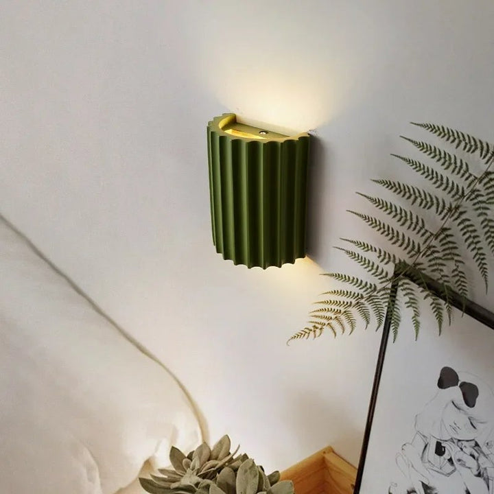 Green wall sconce on a white wall with a plant and artwork in the background