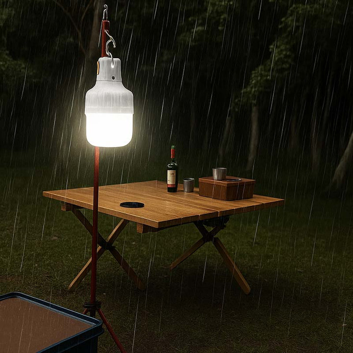 Portable light fixture on a camping foldable table in the rain with a bottle and cups.