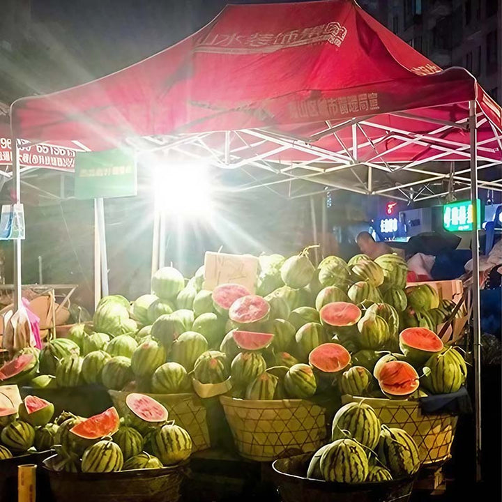 Watermelons displayed under a red tent at an outdoor market.