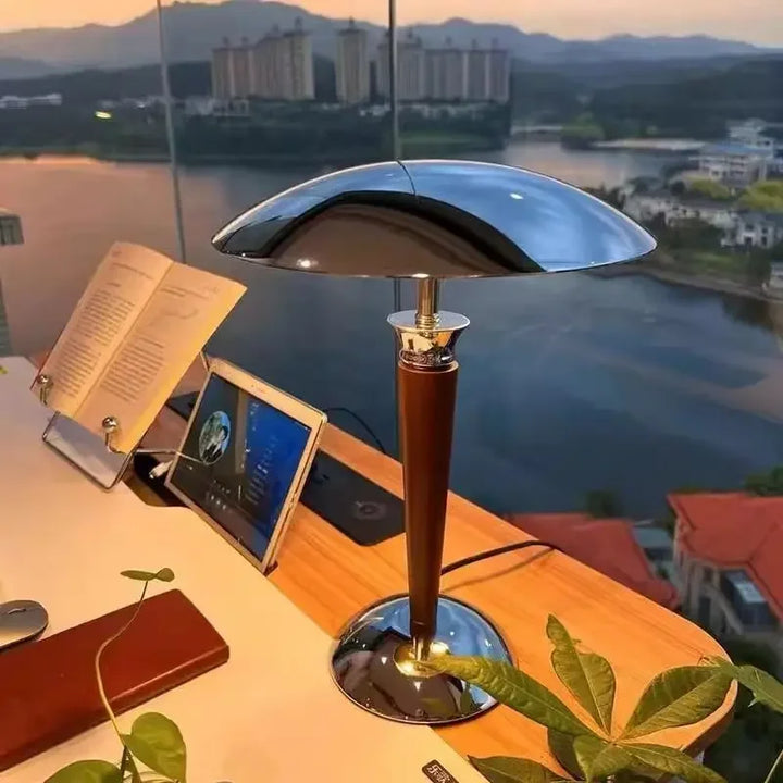 Modern wooden desk lamp with chrome dome shade placed by a window with books