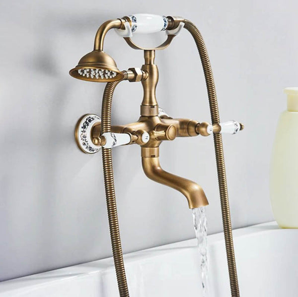 Wall-mounted vintage brass bathtub shower faucet set with handheld sprayer and curved spout, water running into tub.