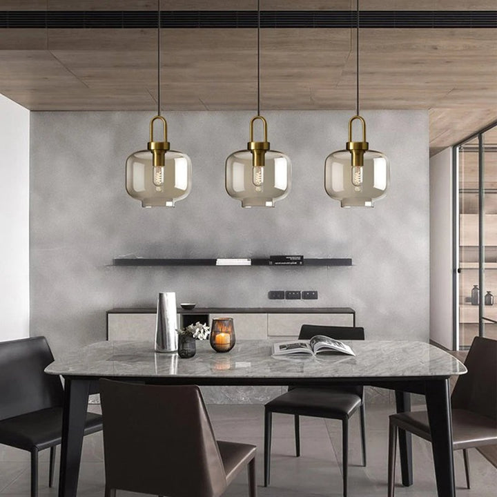 Industrial glass ceiling lamps with brass details hanging above a minimalist UK wood dining table.