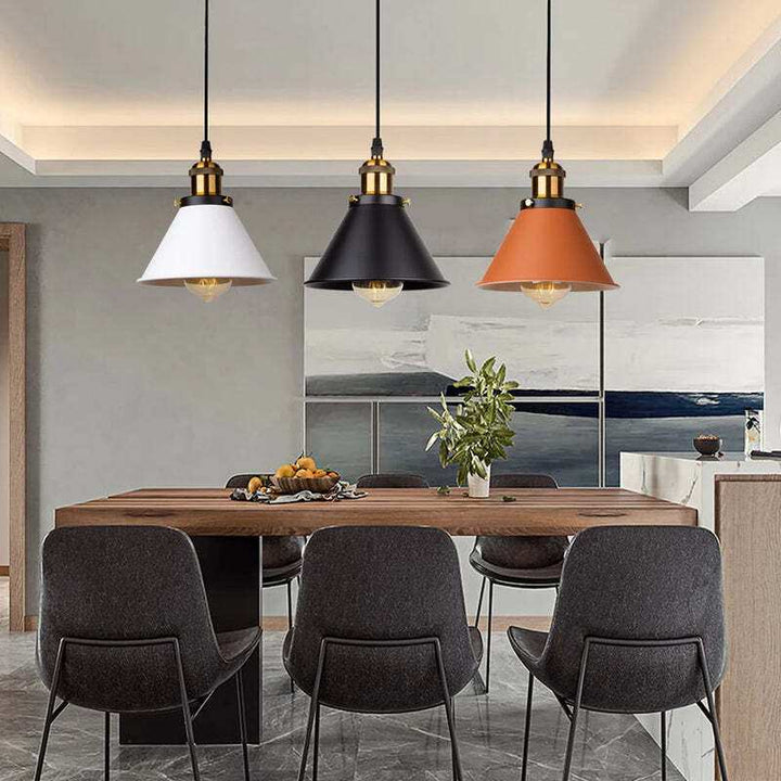 Set of three industrial pendant lamps in black, white, and orange shades hanging over dining table.