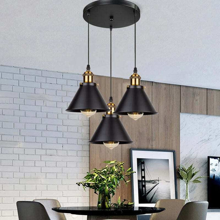 Cluster of three black vintage industrial pendant lamps with brass detail in dining room.