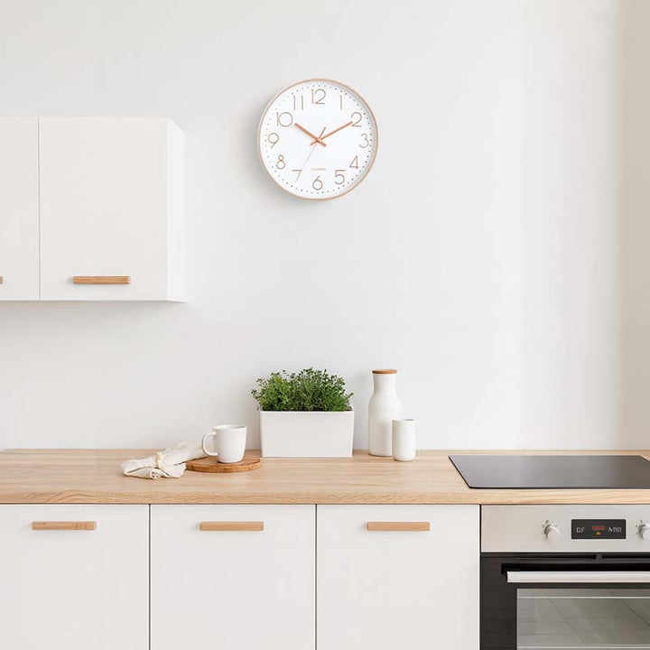 Modern kitchen with a white and gold wall clock on the wall, wooden countertop, and white cabinets.