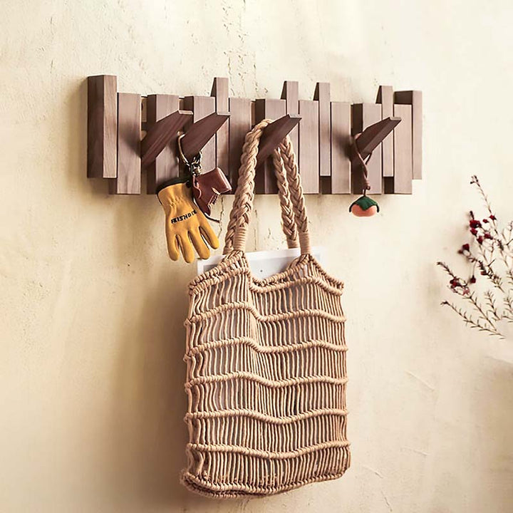 Wooden wall hook with a woven bag and gloves on a beige wall.
