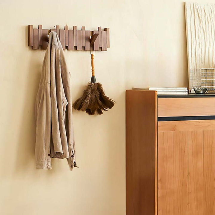 Wooden wall hook with a coat and broom on a beige wall next to a wooden cabinet.