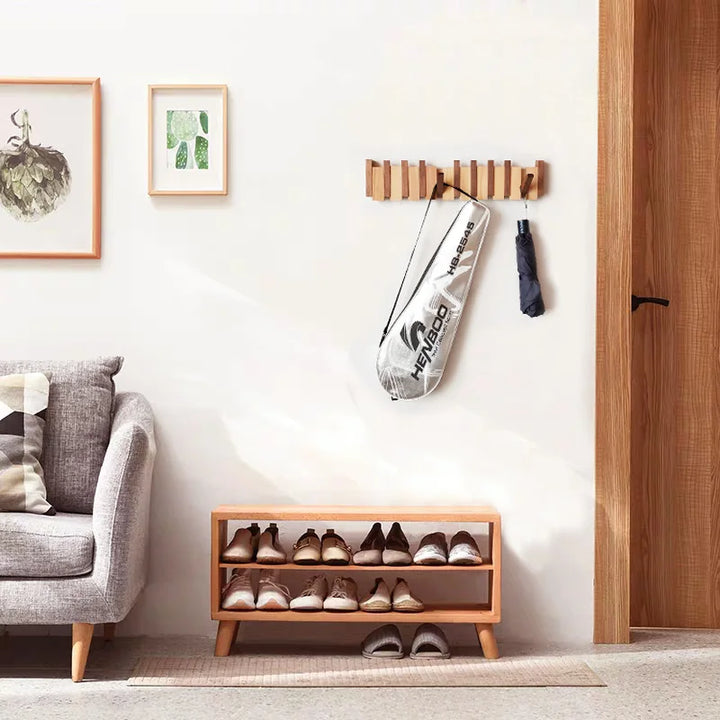Wooden shoe rack with shoes underneath, umbrella, and coat hook on a white wall with a gray sofa.
