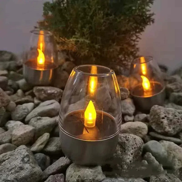 Solar LED candle lights with stainless steel base and warm amber glow, set on outdoor stones for garden decor.