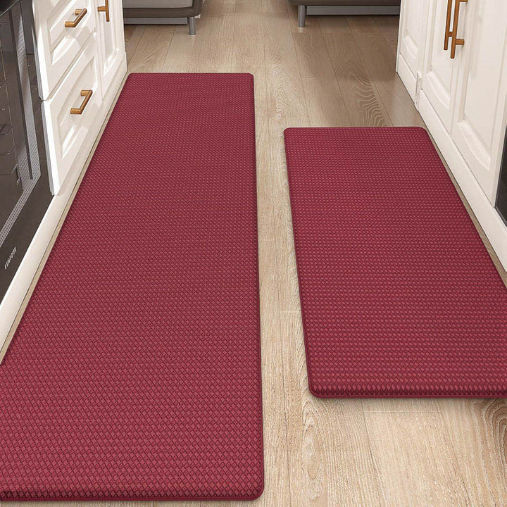Two red kitchen mats on a wooden floor with white cabinets in the background.