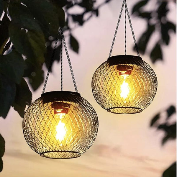 Pair of decorative outdoor solar lanterns with warm LED light, hanging on tree branches at sunset.