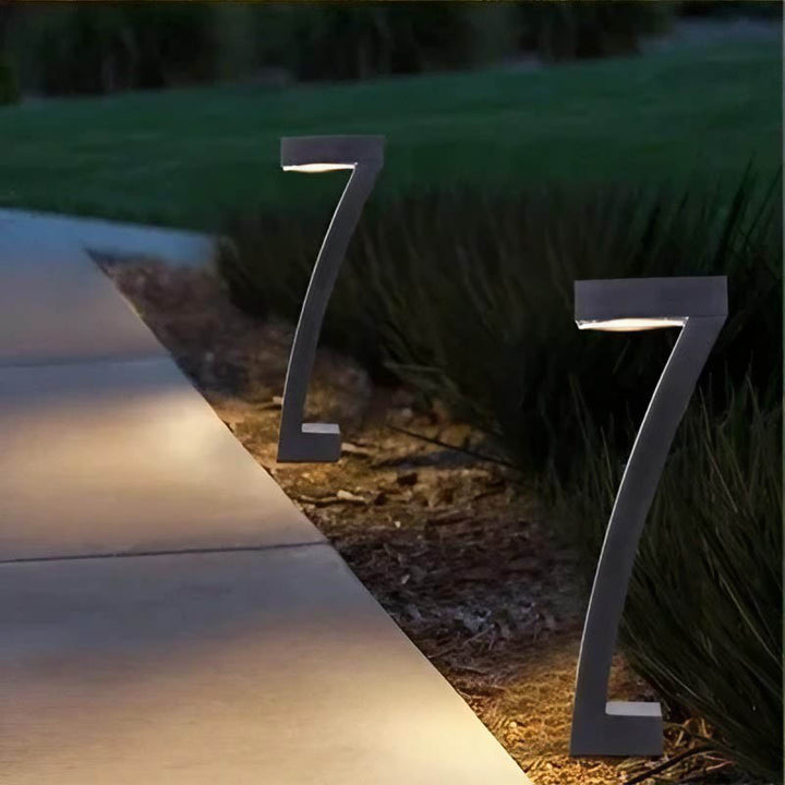 Black 7-shape modern solar garden light casting warm LED glow on a stone pathway at dusk