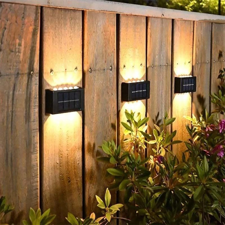 Solar-powered LED wall lights mounted on wooden garden fence, casting warm waterproof glow for outdoor walkway decor.