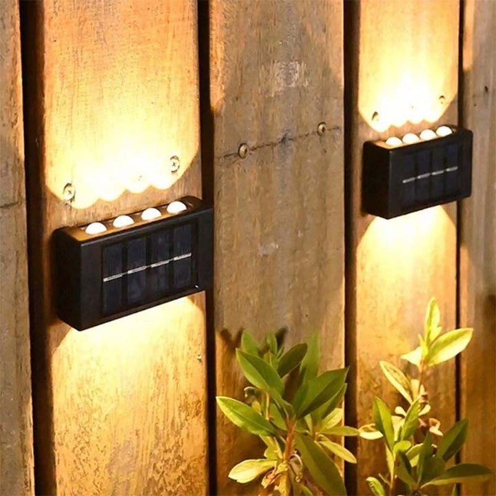 Warm white solar wall lights highlighting wooden fence and garden plants—decorative outdoor lighting solution.